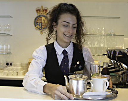 Waiter woman arranges a teapot and drinks onto a tray. 