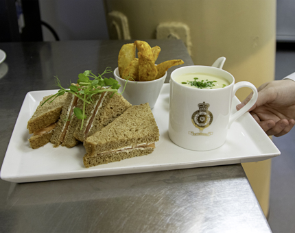 A salmon sandwich, mug of soup and potato wedges on a platter ready to be served. 