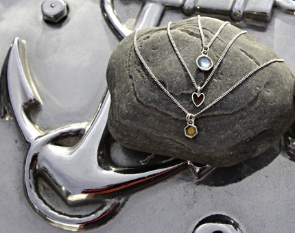 Three delicate organically-shaped necklaces are displayed on a stone. 