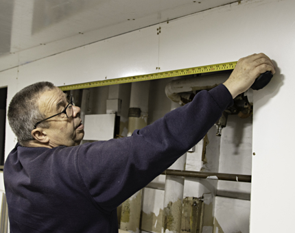 Maintenance man holds up a tape measure against a wall. 