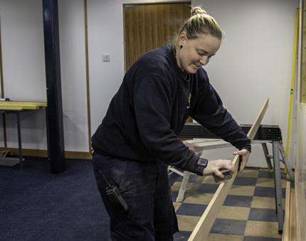 Maintenance woman sands a long plank of wood in Britannia's Training Room. 