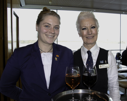 Members of the Royal Deck Tea Room team stand smiling, holding a tray containing two glasses of wine.