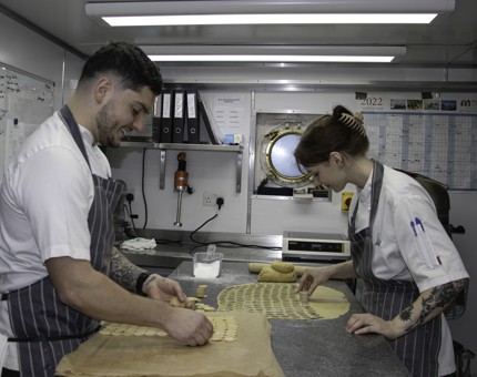 Two chefs cut out shortbread round shapes in the Galley. 