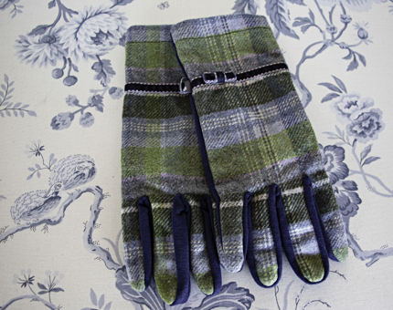 Blue, green and purple coloured tartan wool gloves sit on a blue and white printed background. 