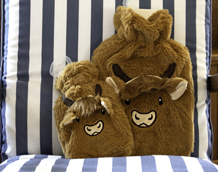 A large and a small novelty furry hot water bottle with a Highland cow's face on the front.