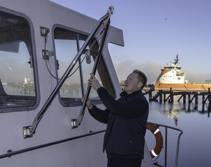 Man inspects a metal winch affixed to the side of Royal Nore. 