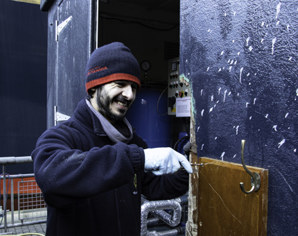 Maintenance man uses a screwdriver to replace a wooden panel on a door in the pumphouse on the Quayside.