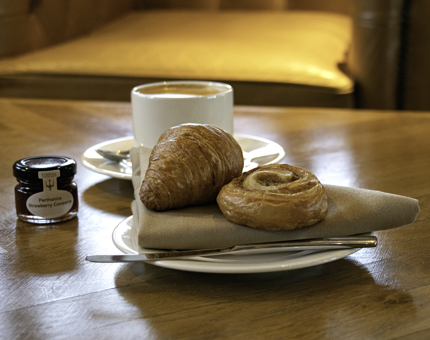 A selection of breakfast pastries are on a plate with a mug of coffee and small pot of jam. 