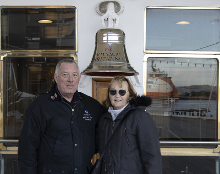 Couple stand smiling next to Britannia's Bell. 
