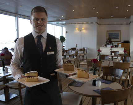 A Waiter holds plates containing large slices of three different cakes in the Tea Room. 