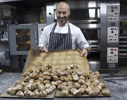 Chef holds a large tray of baked bread rolls. 