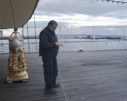 Maintenance team member holding a string of lights as he arranges them on the outside of the Verandah Deck.