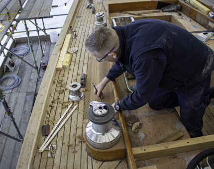 Man holding a pencil as he measures up a length of wood on deck. 