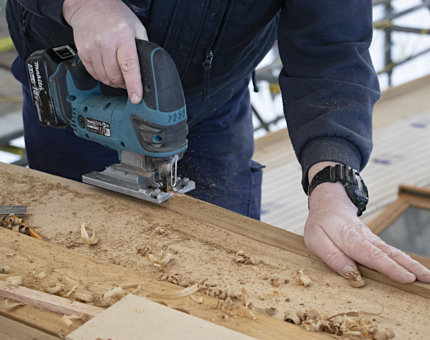 Maintenance team member holding a power tool cutting wood. 