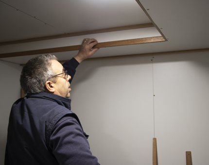 Man fitting beading on the wall near the ceiling in the Training Room.