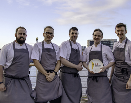 Five chefs stand outside on Fingal's deck as one holds The AA Rosette Award for Culinary Excellence. 