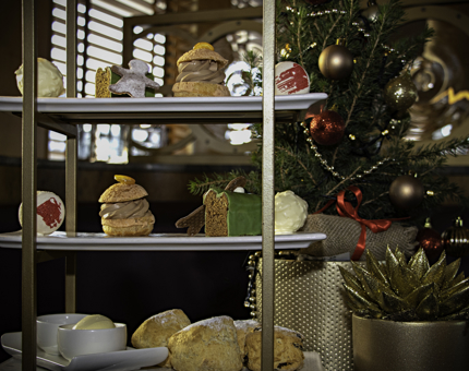 A tiered cake stand containing sweet festive Afternoon Tea miniature treats. A Christmas tree is in the background.