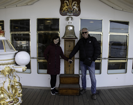 Two visitors stand either side of Britannia's Bell smiling. 