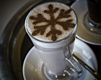 A tall glass of hot chocolate with a stencil snowflake on top. 