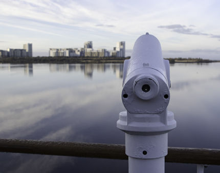A telescope on deck looking out across a waterfront view.
