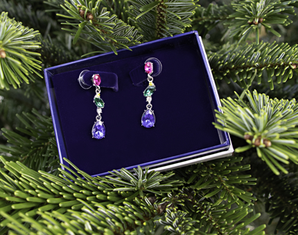 Blue, green and pink drop earrings in a gift box next to a Christmas tree. 