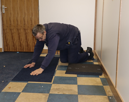 Man from the Maintenance Team laying down carpet tiles. 