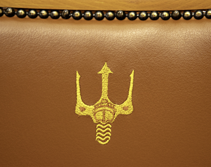 Close-up detail of Fingal's trident logo on a brown leather armchair back.