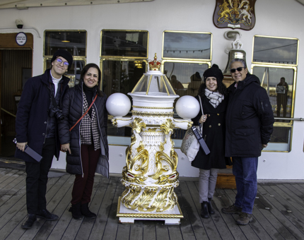 Four people stand next to Britannia's ornate large white and gold compass binnacle. 