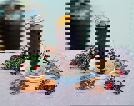 A tall glass of mulled wine decorated with a twist of orange peel and cinnamon sticks.