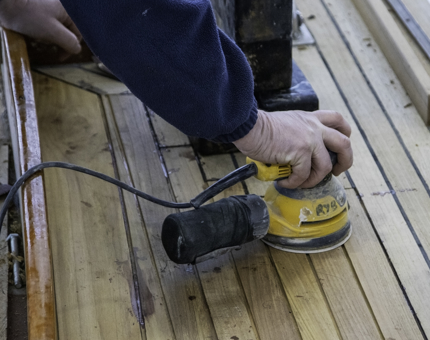 Man holds a sander as he sands the deck timbers on Bloodhound. 