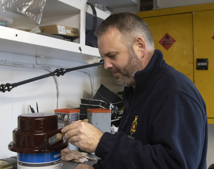 Maintenance man painting a trophy base with brown varnish.