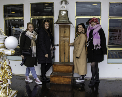 A group of four people stand next to Britannia's large bell. 