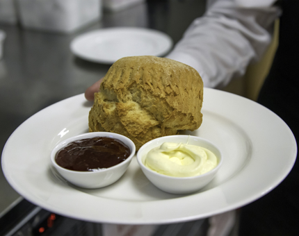 A plain scone on a plate with strawberry jam and clotted cream on a plate.