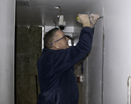 Maintenance man holds a chisel in the Quarter Galley removing plasterboard.