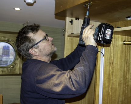 Maintenance team member holds a drill as he removes a wardrobe within a cabin at Fingal.
