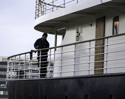 Man removes varnish from a handrail on the outside deck at Fingal.