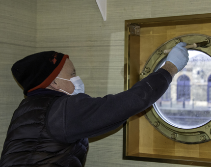 Maintenance man paints a porthole window. 