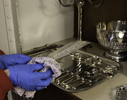 A close-up of a Housekeeper polishing silver cutlery.