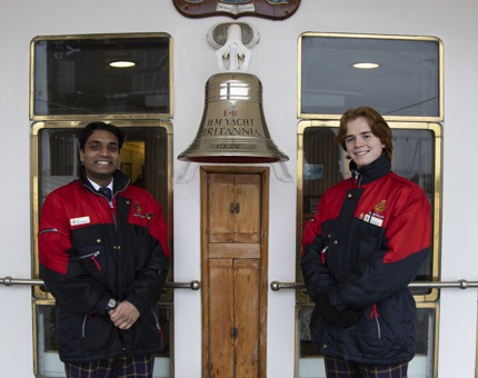 Two Visitor Assistants stand next to Britannia's bell. 