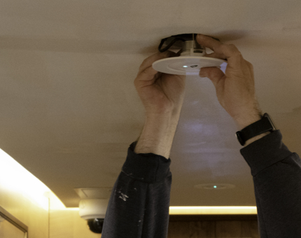 A man returns a light fitting to its ceiling placement following painting works. 