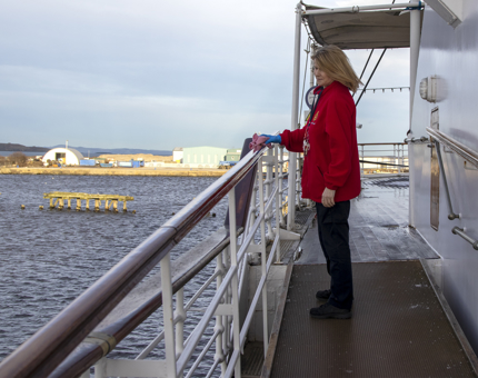 Housekeeper stands outside on deck polishing a handrail. 