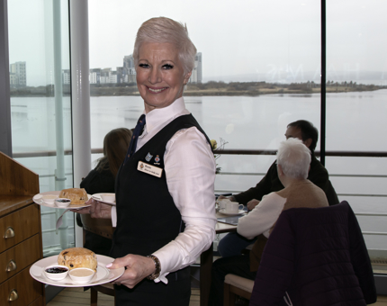 Waiter holds two trays of scones, clotted cream and jam. 