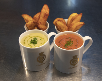 Two mugs of soup and pots of potato wedges. 
