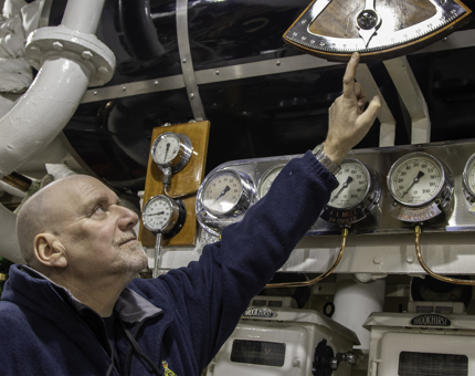 Team member in Maintenance pointing to the inclinometer in Britannia's Engine Room.