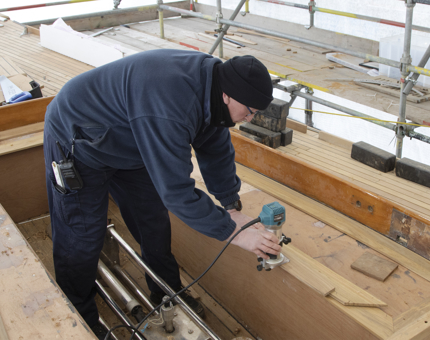 Maintenance man routering deck timbers on Bloodhound. 