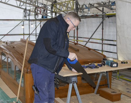 A man saws teak deck timber on Bloodhound. 