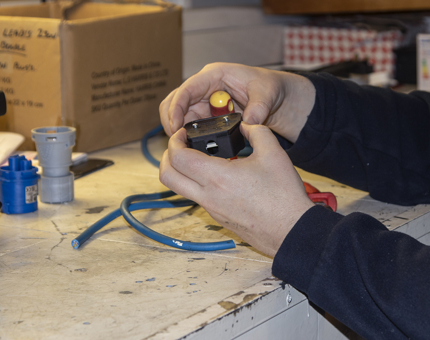 A member of the Maintenance team holds a plug to make up a bespoke extension lead.