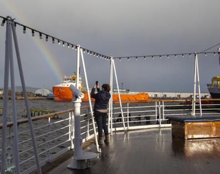 A visitor standing on the Verandah Deck photographs a rainbow. 