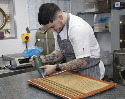A Chef piping coffee eclairs in the pastry galley. 