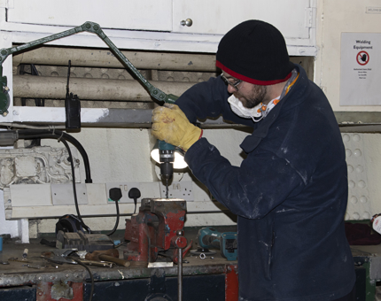 Team member in Maintenance holding a drill in the workshop to make support brackets. 